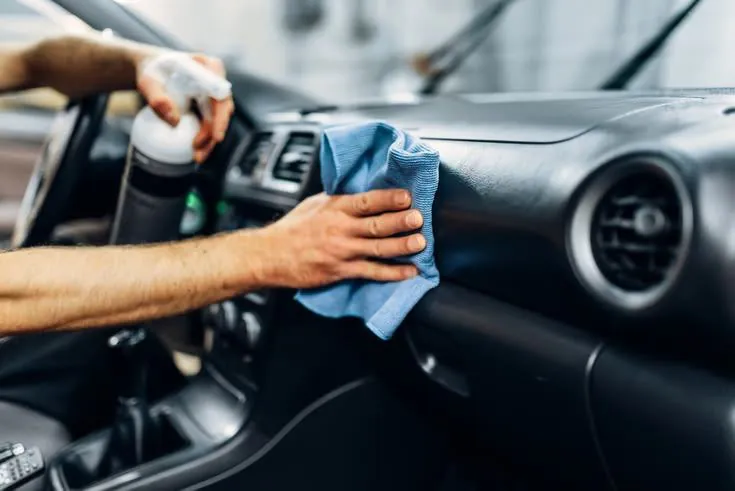 Technician wiping a car dashboard with a blue microfiber cloth