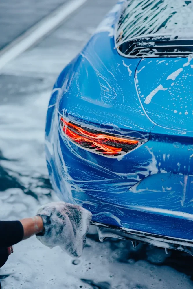 Hand washing a blue car with a soapy mitt