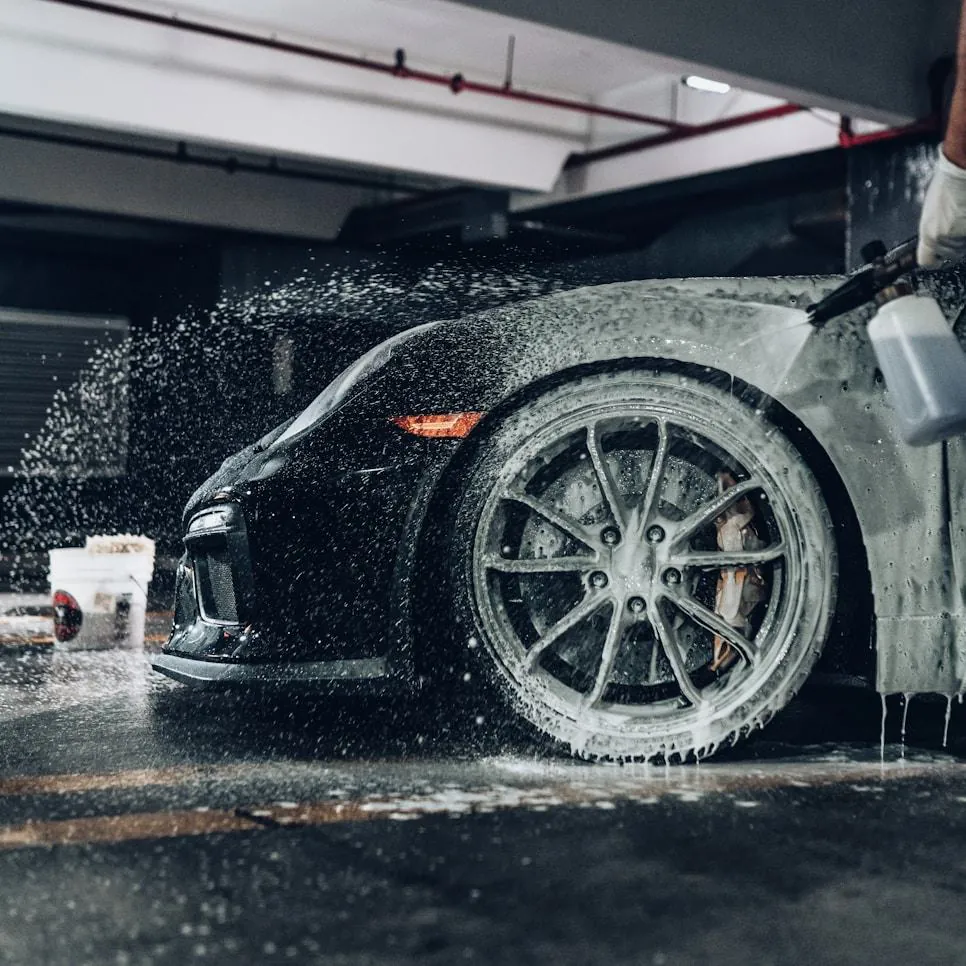 Foam being rinsed off the wheel of a dark sports car
